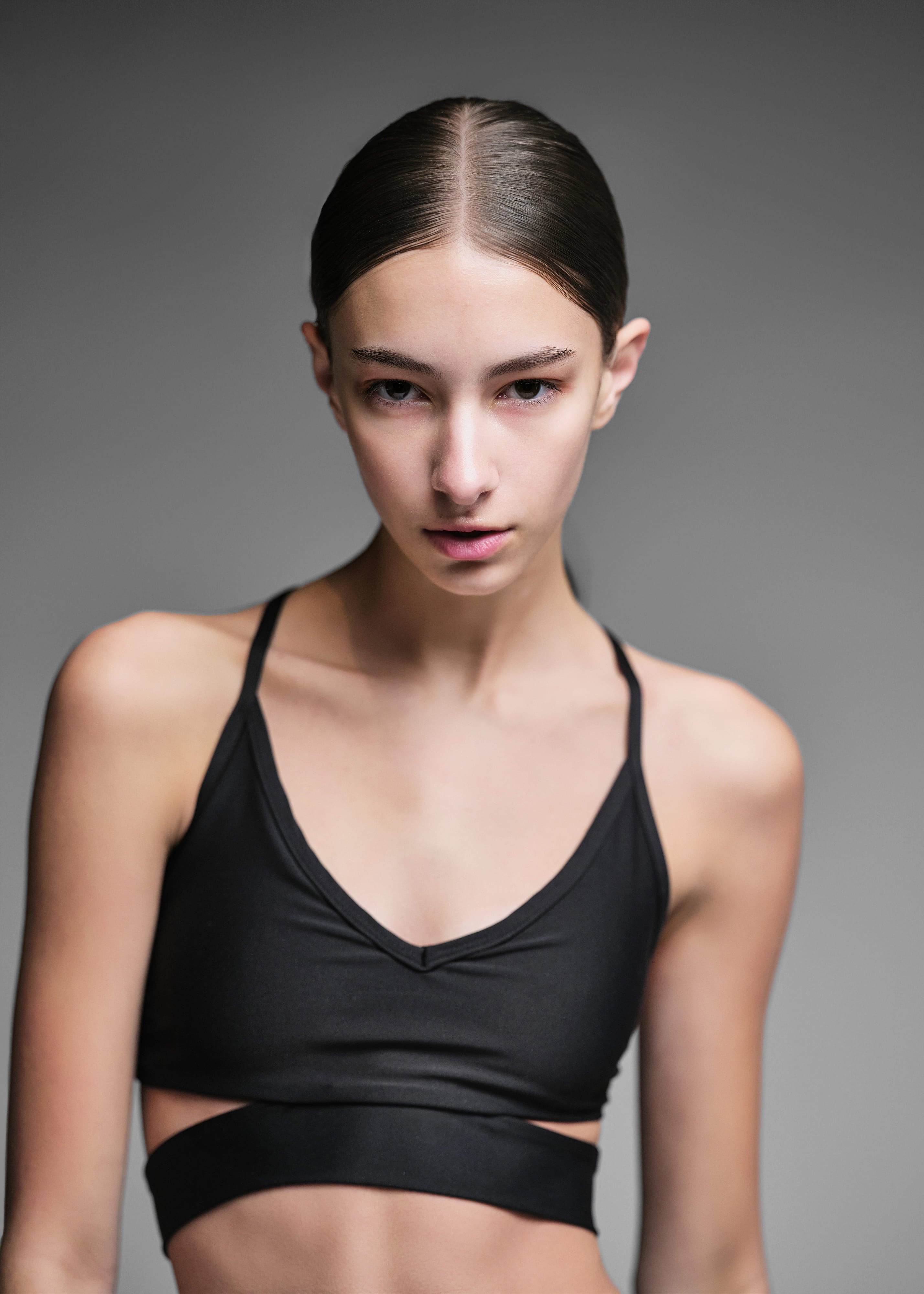 Ava Ecker with her hair slicked back, looking into the camera, grey seamless