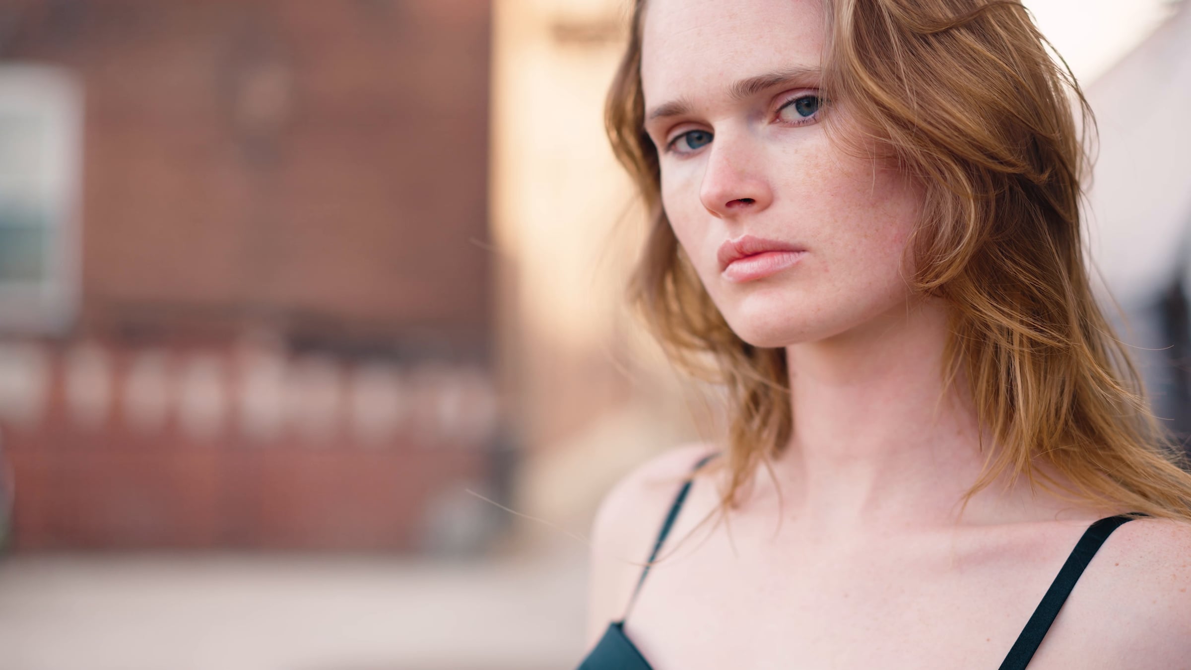 Close-up of Kate Wiggins looking toward the camera, warm light and a softly blurred brick background, from her fashion film
